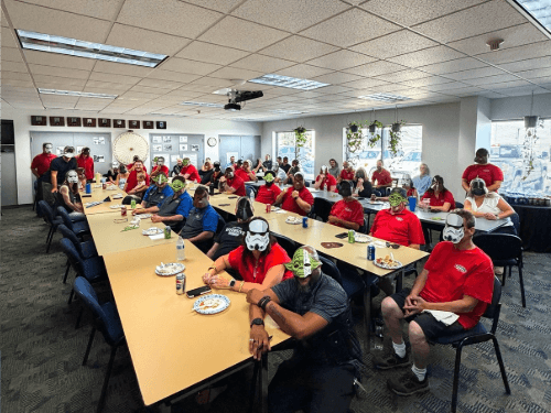 Large group of Wendle employees seated at tables wearing Star Wars masks during a festive team gathering event.