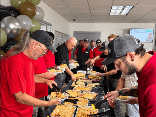 Wendle Nissan employees lining up at a buffet table serving hot food during a staff 25th anniversary party.
