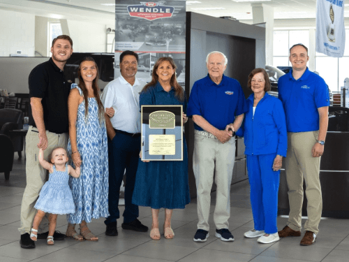 Wendle family members posing indoors together while proudly holding the President's Award plaque.