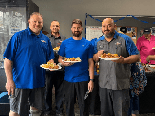 Wendle team members smiling and holding plates of food together during an indoor office celebration event.