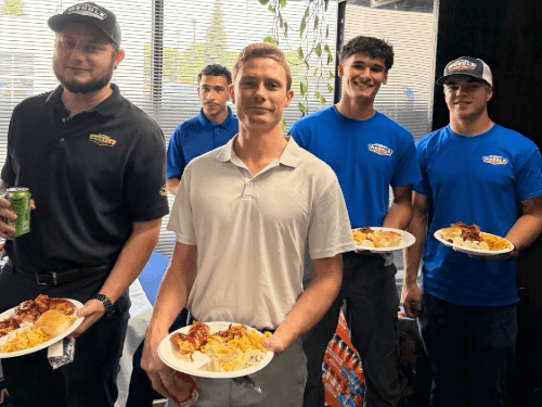 Wendle team members posing with plates of food and drinks during an indoor office celebration event.