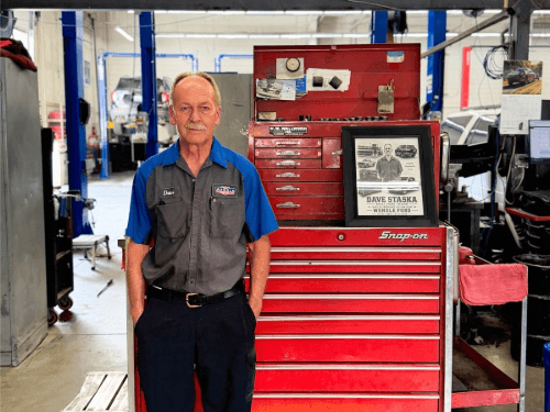Dave Staska standing proudly next to his red tool chest and retirement plaque in the Wendle Ford service department.