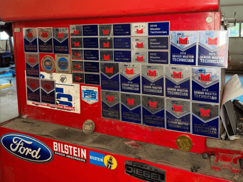 Close-up of a red mechanic tool chest displaying numerous Ford Master Technician awards and badges.