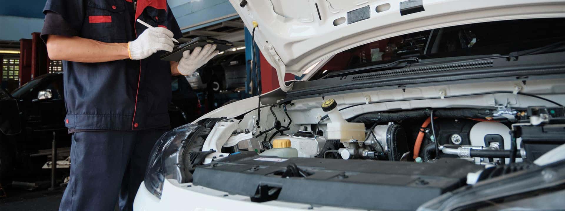 technician servicing a hybrid car with hood up showing batteries